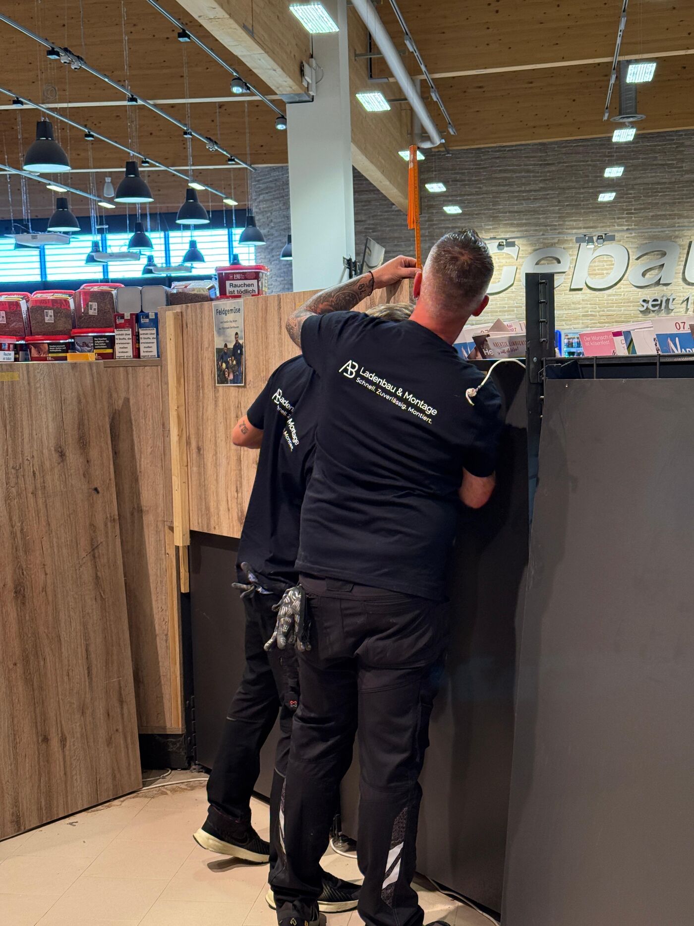 Zwei Monteure von A.B. Ladenbau und Montage beim Aufmaß an der Kassenzone
